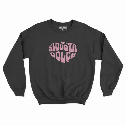 Dessuadora negra amb el disseny “Xiqueta Dolça” al pit en tipografia retro groovy rosa amb forma de cor, de Canya de Sucre.