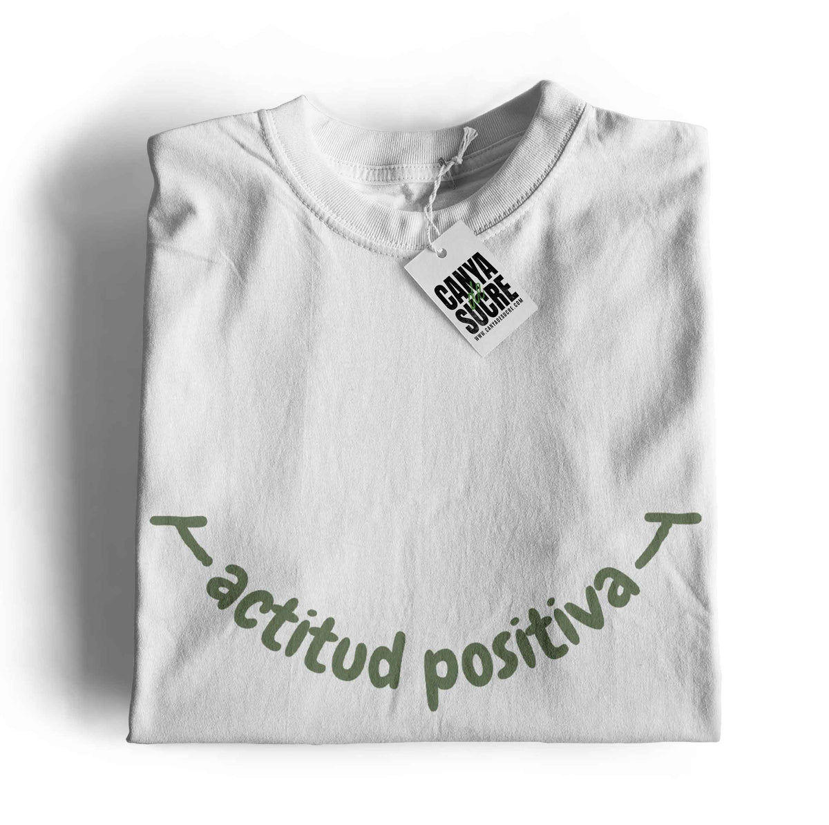 Samarreta color blanc amb la frase actitud positiva en verd al pit formant un somriure. Disseny de Canya de Sucre