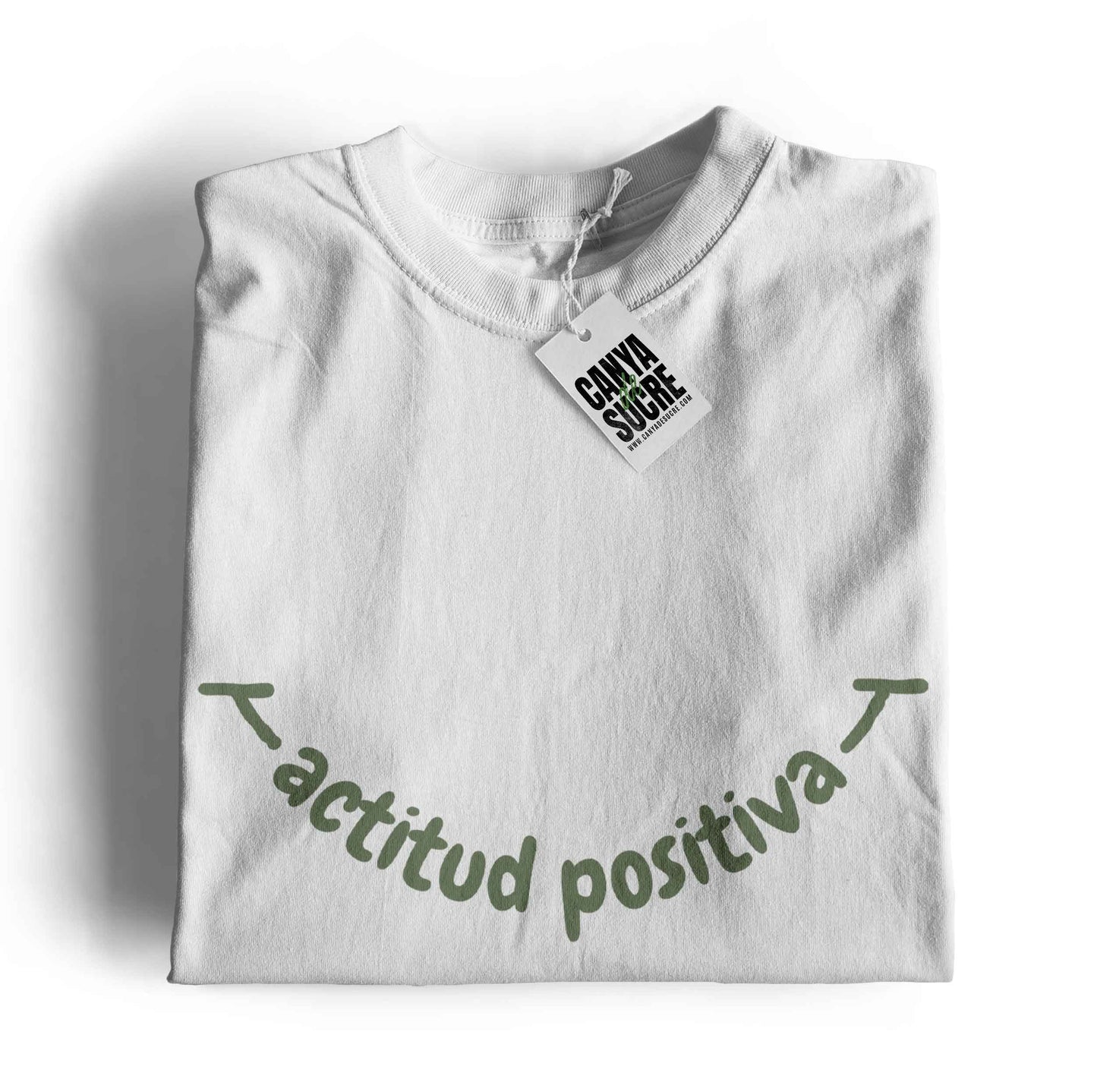 Samarreta color blanc amb la frase actitud positiva en verd al pit formant un somriure. Disseny de Canya de Sucre
