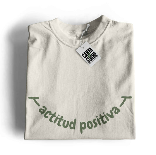Samarreta color blanc vintage amb la frase actitud positiva en verd al pit formant un somriure. Disseny de Canya de Sucre