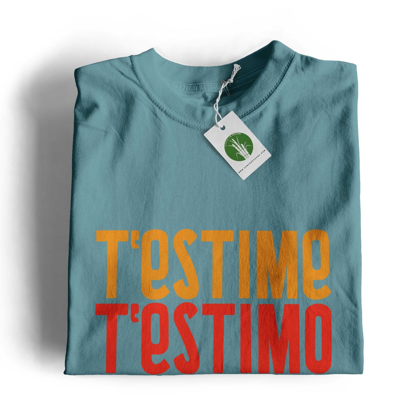 Samarreta infantil color blau dusty plegada amb etiqueta de Canya de Sucre i el text “T’estime” en tons grocs i rojos i verds.