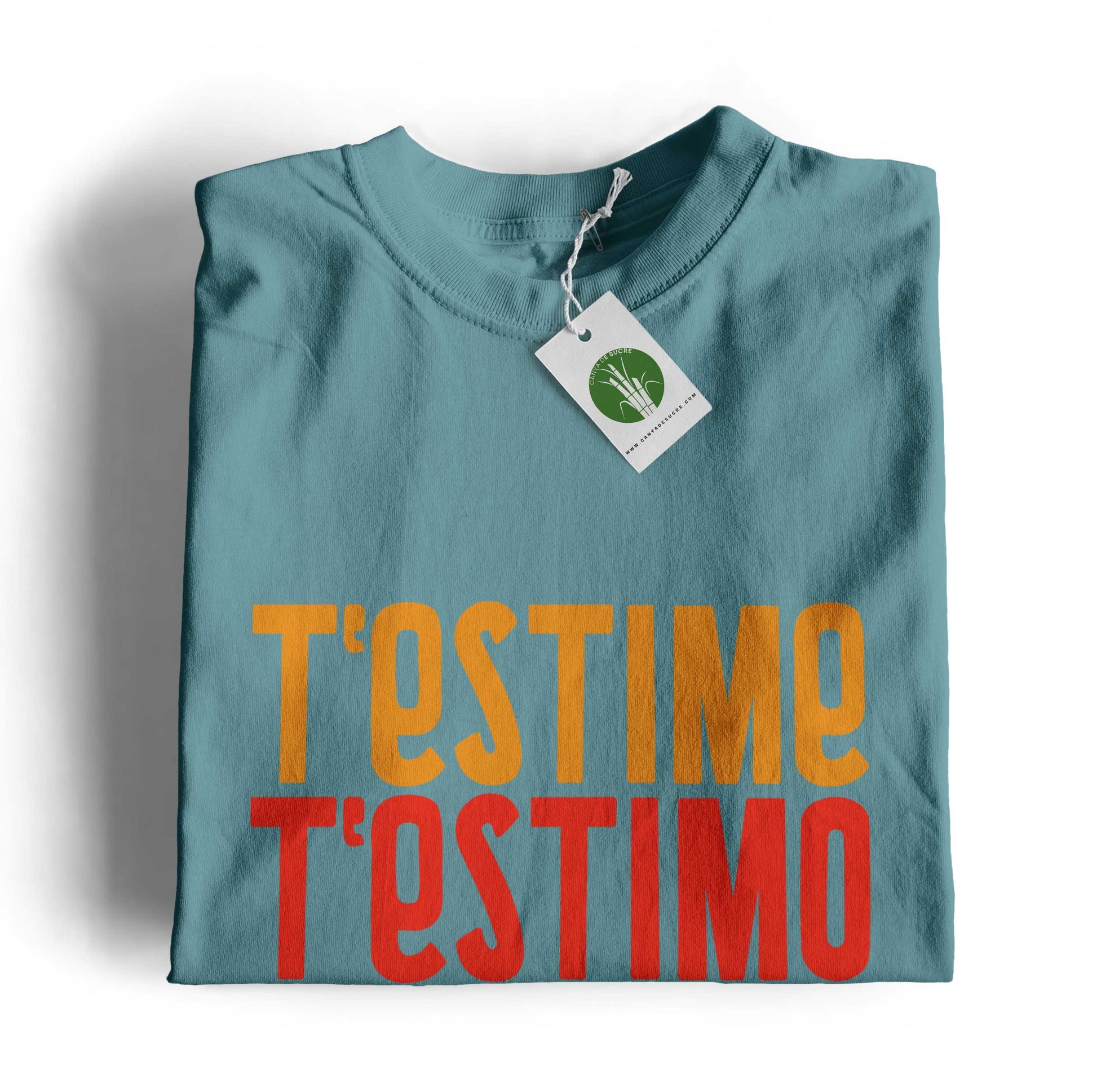 Samarreta infantil color blau dusty plegada amb etiqueta de Canya de Sucre i el text “T’estime” en tons grocs i rojos i verds.